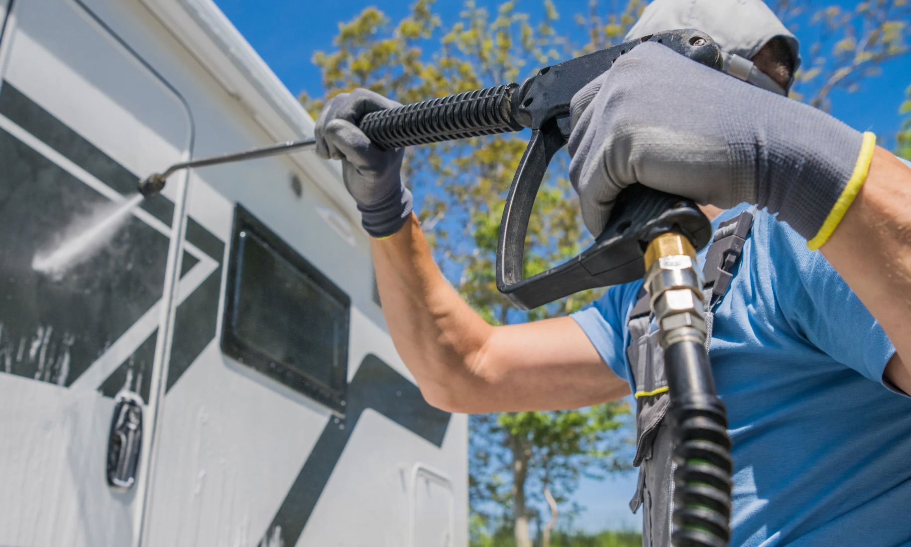 pressure-washing Commercial Pressure Washing - All In House LLC in Tualatin, OR: Person pressure washing a white RV in sunny weather, wearing gloves and a blue shirt.