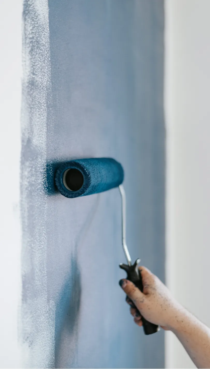 commercial-painting-3 (1) A hand using a roller to paint a wall blue.