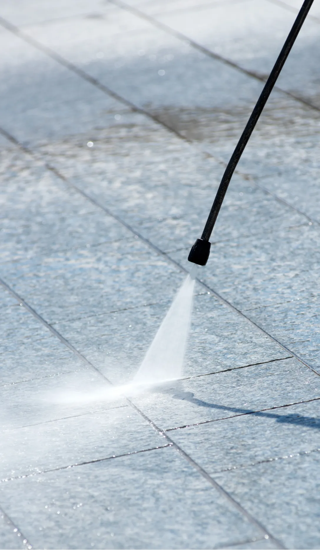 commercial-pressure-washing-2 (1) Close-up of a pressure washer cleaning a tiled outdoor surface with a strong water jet.