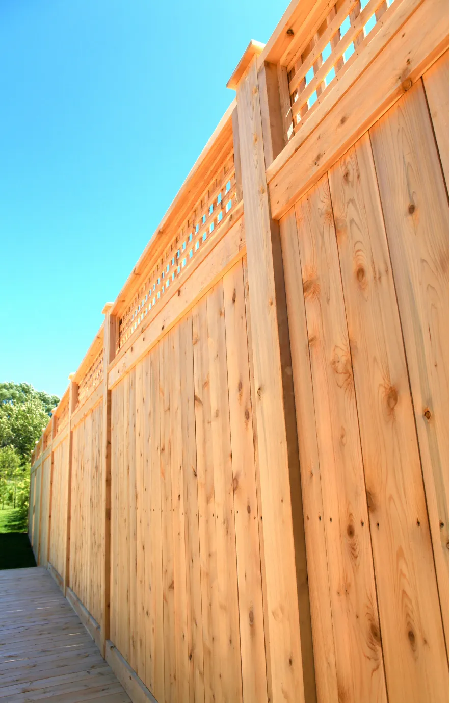 fence-installation-2 Tall wooden fence with decorative lattice top, set against a clear blue sky and greenery in the background.