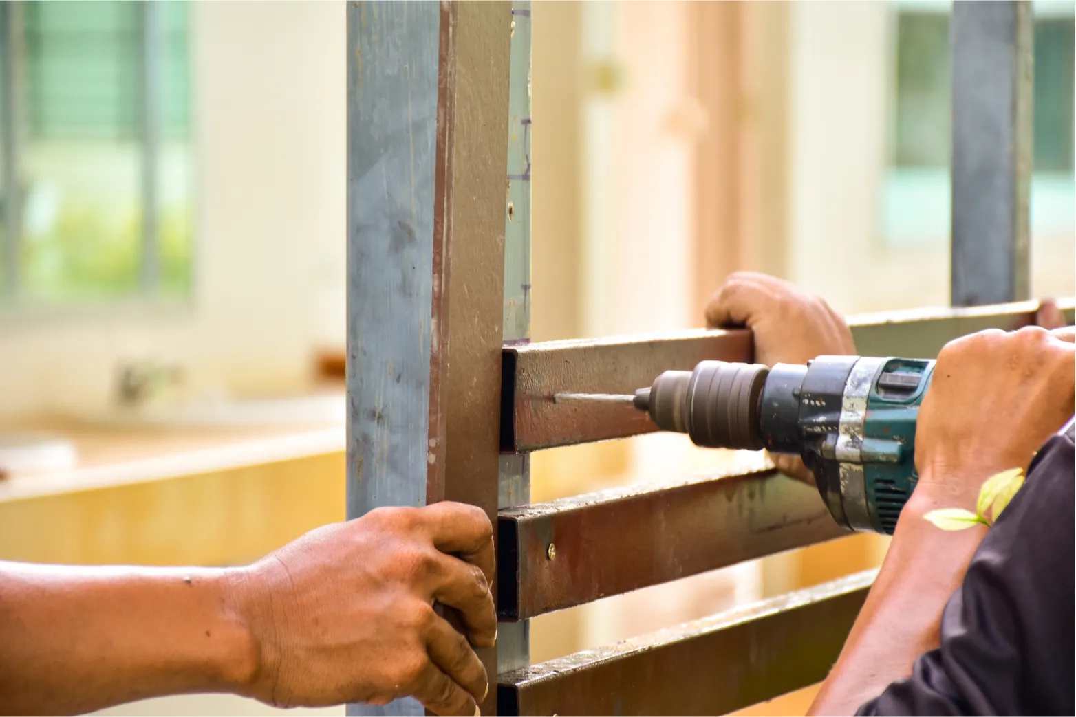 Two people working with a power drill on a metal frame indoors.