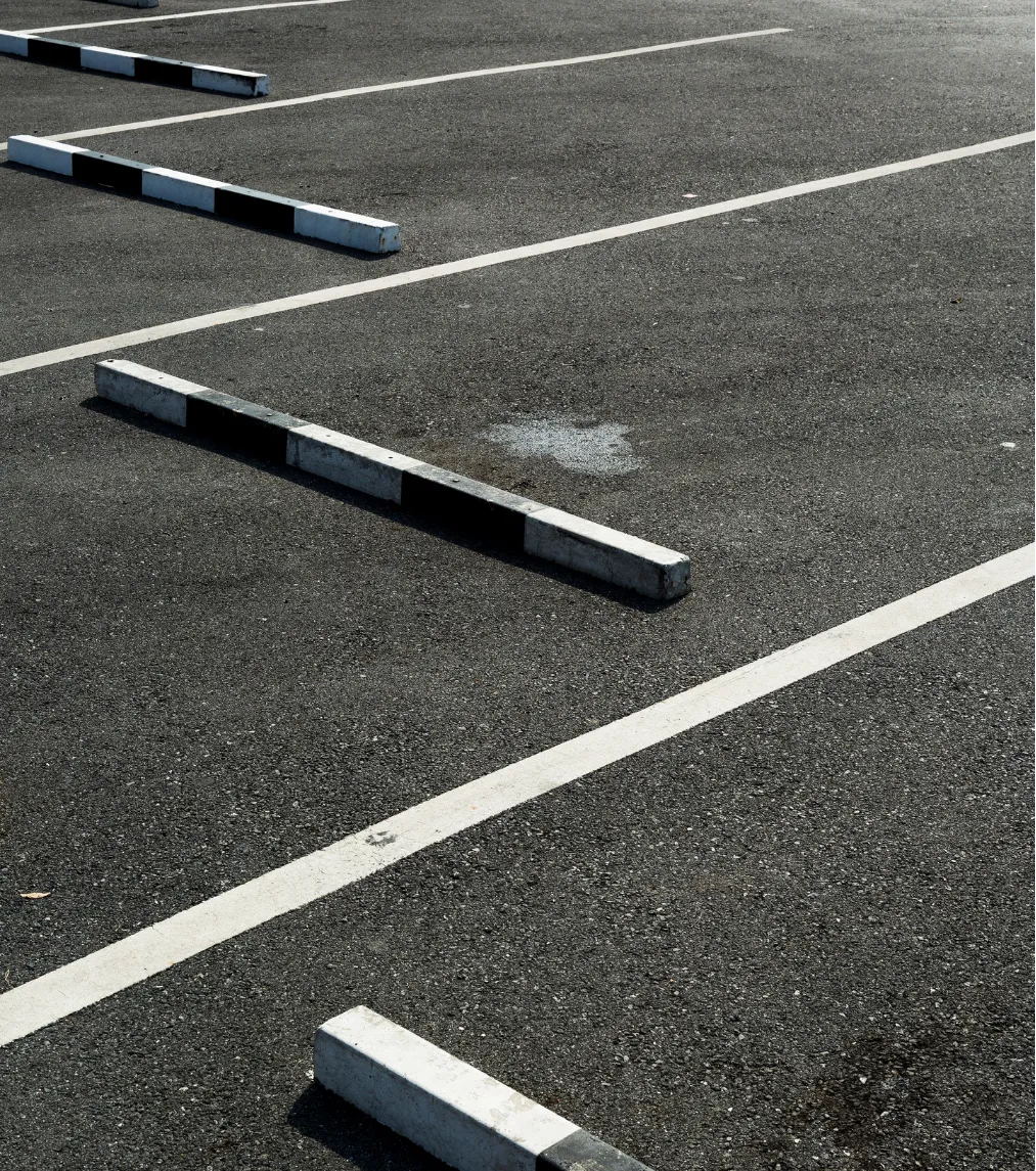 line-striping-4 Empty parking lot with marked spaces and black-and-white striped concrete barriers on an asphalt surface.