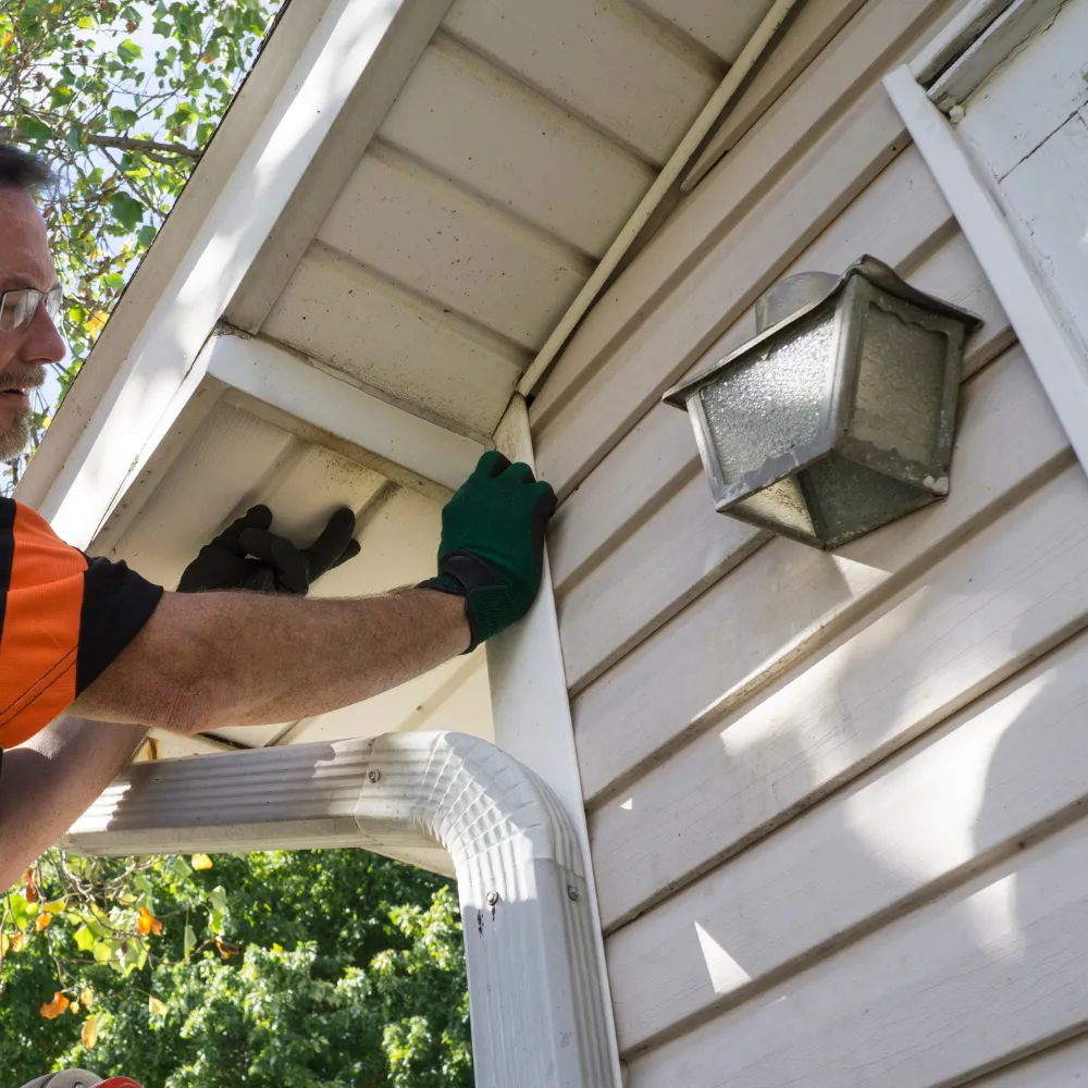 siding-repair Person in gloves installing siding on a house using a ladder, with a nearby outdoor light fixture.